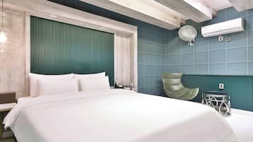 A modern hotel room with a large bed, a green accent wall, a round table, and an air conditioning unit.