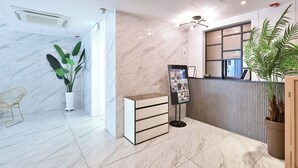 A modern reception area with marble flooring, a reception desk, a potted plant, a wall-mounted information board, and a seating area with a chair. - Gyeongju hotel namu (Gyeongju)