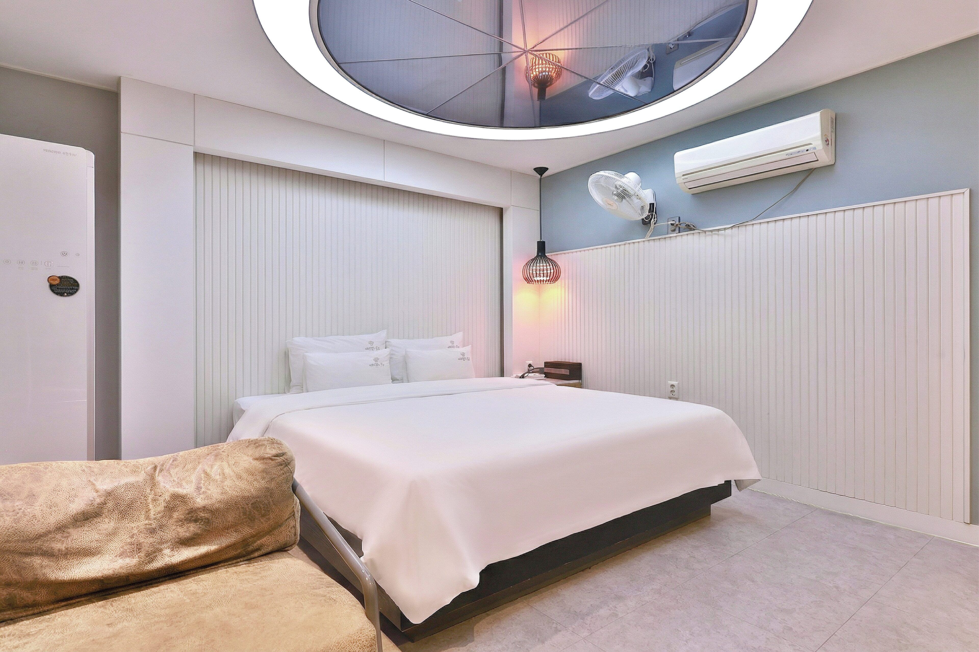 A modern bedroom with a bed, a bedside table, a wall-mounted air conditioner, and a ceiling light fixture.
