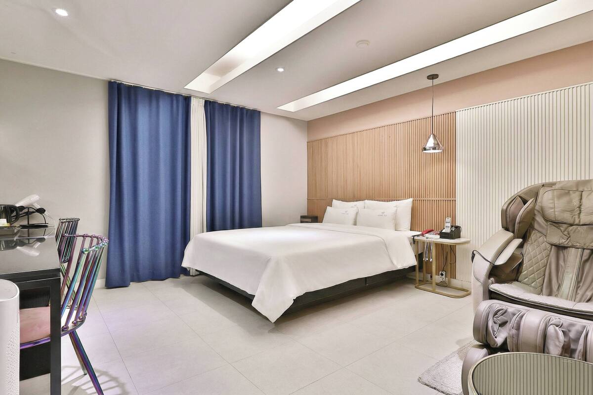 A modern hotel room with a bed, a desk, a chair, and a massage chair.