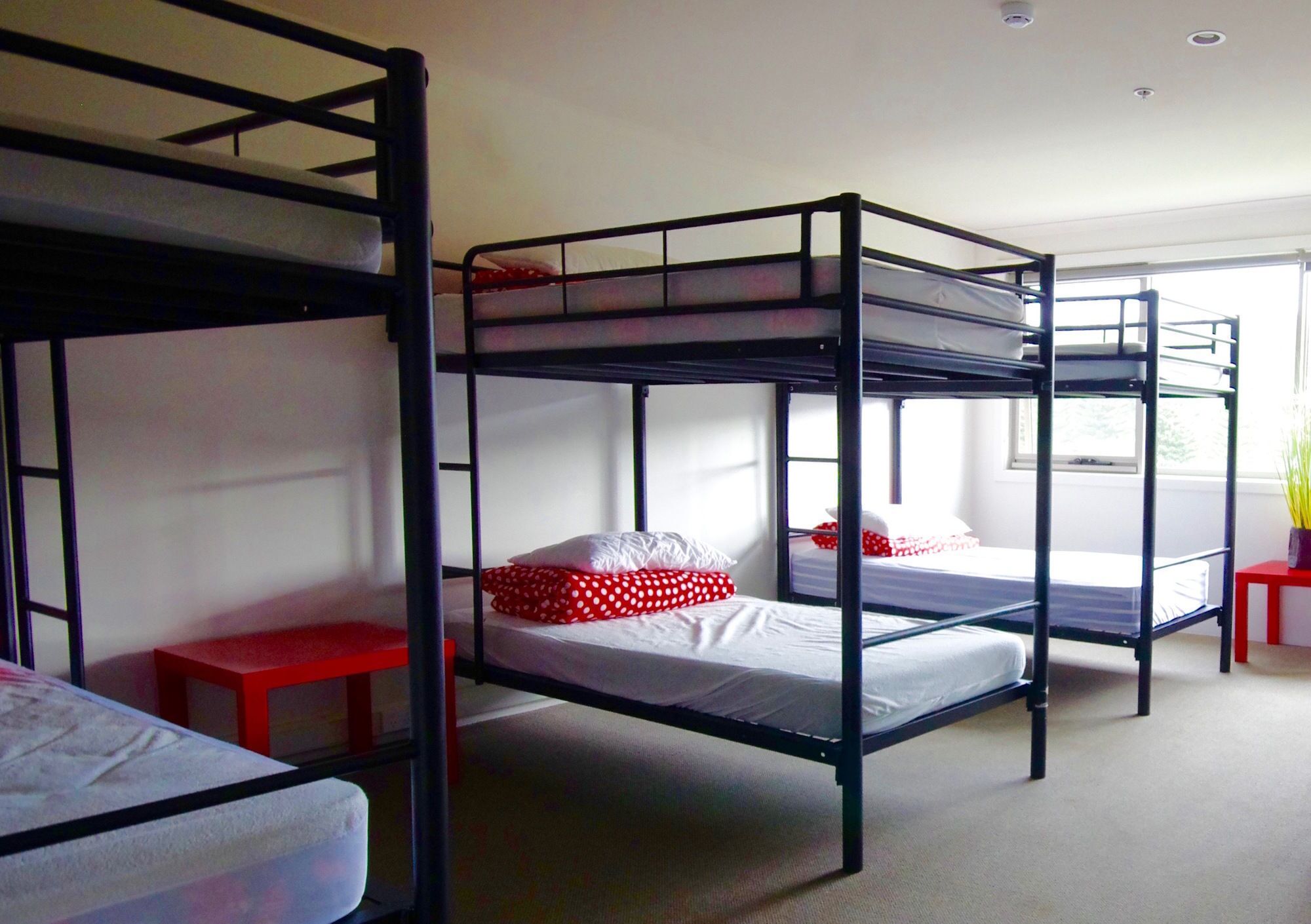 A dormitory room with bunk beds, a red stool, and a small table.