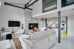 A modern living room with a stone fireplace, a flat-screen TV, and a staircase leading to an upper level. - Parisian Duplex - Montorgueil - Central Paris (Paris)