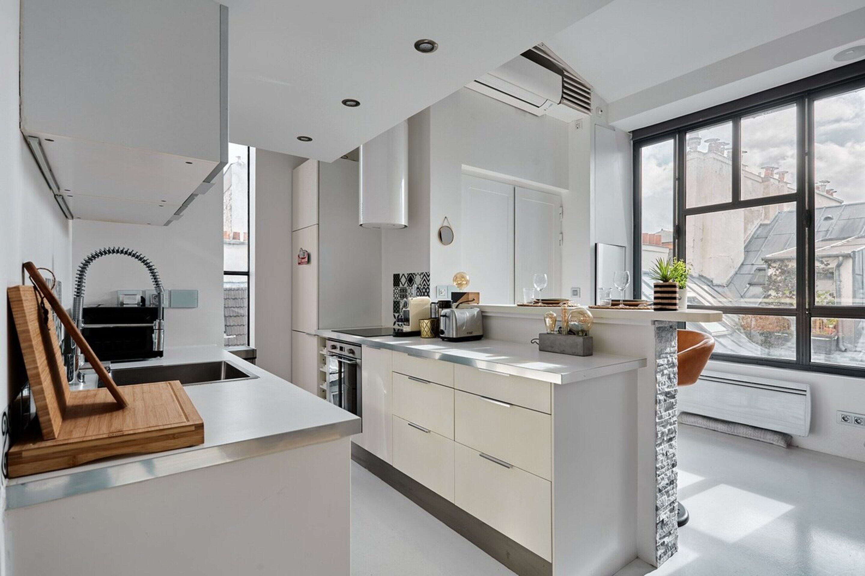A modern kitchen with white cabinetry, a central island, and a large window providing a view of the cityscape.
