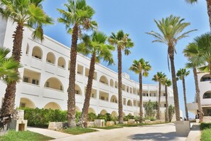 A multi-story hotel with a symmetrical facade, palm trees, and a clear sky. - Futura Club Barone di Mare (Melendugno)