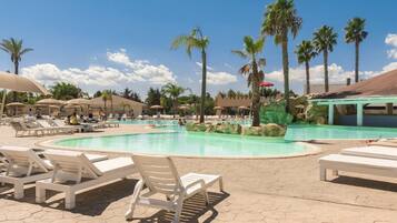 Area piscina con lettini, palme e zona relax coperta.