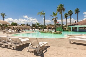 Area piscina con lettini, palme e zona relax coperta.