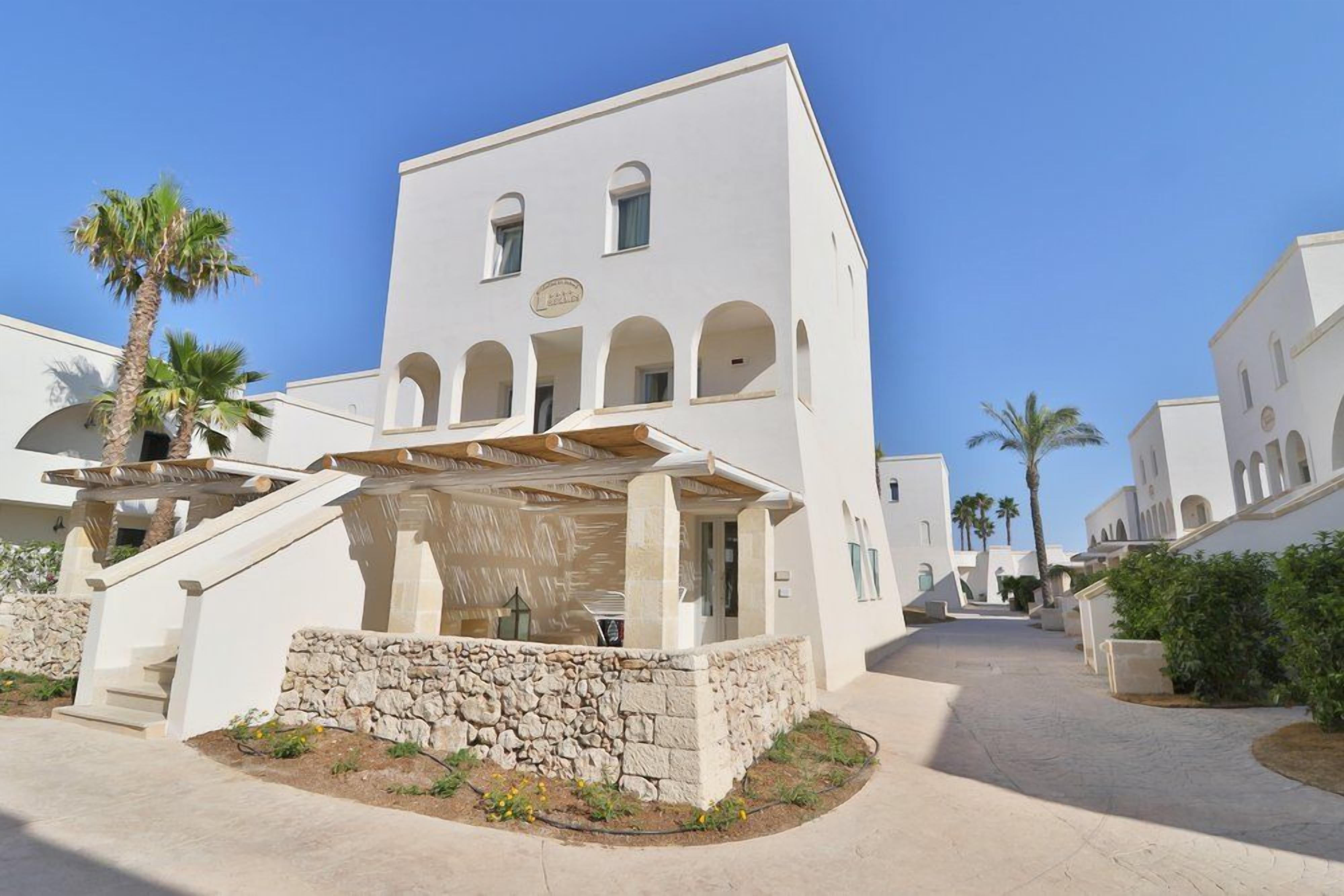 A white building with arched windows and a stone wall in front.