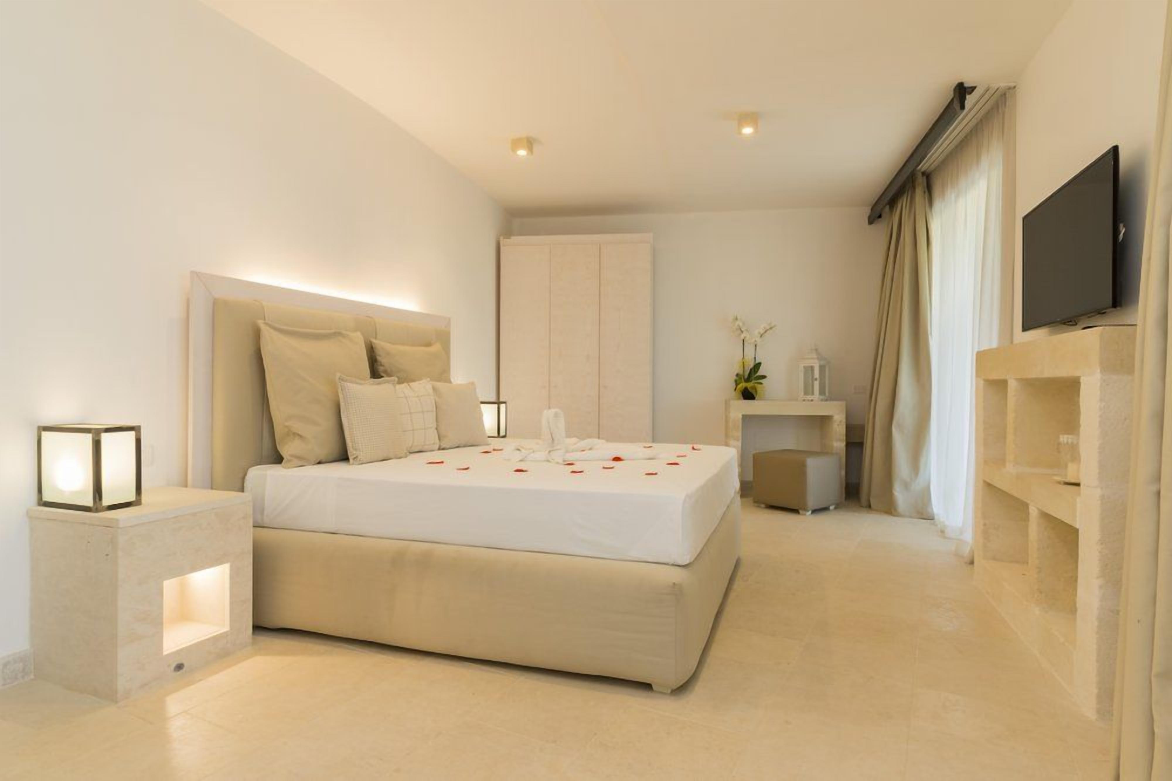 Una camera d'albergo moderna con un letto grande, comodini, una TV a schermo piatto e un piccolo tavolino con una lampada.