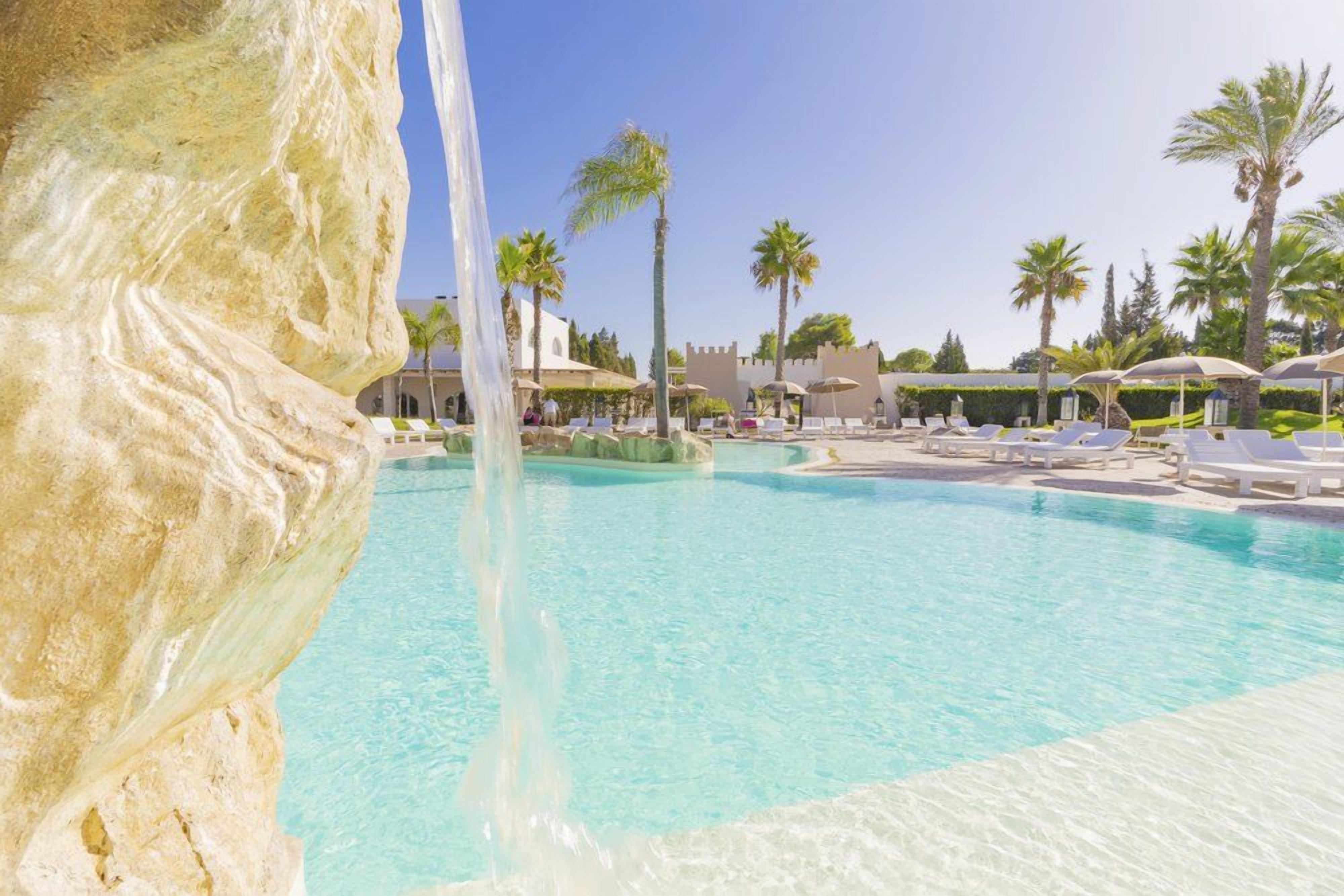 Una piscina con agua cristalina, rodeada de sillas de descanso y palmeras.
