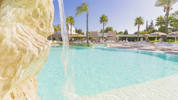 A pool with clear water, surrounded by lounge chairs and palm trees. - Futura Club Barone di Mare (Melendugno)