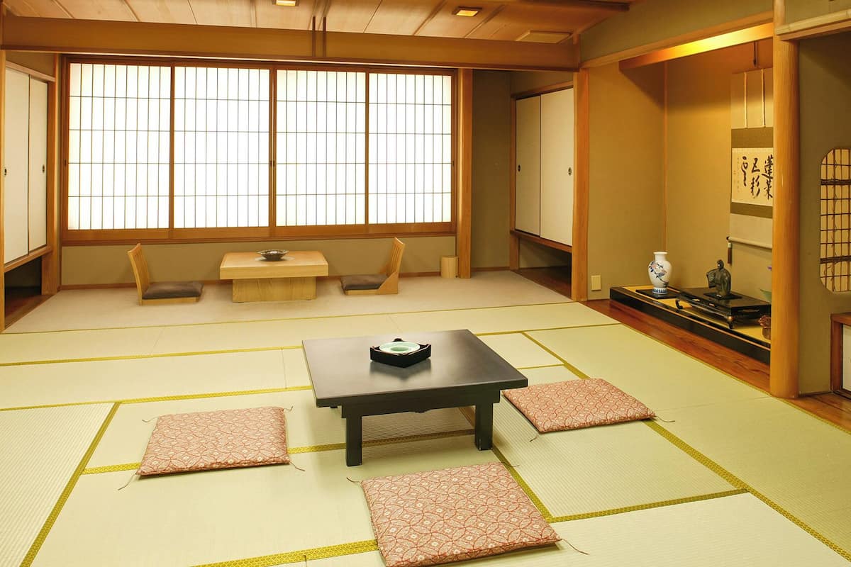 Una habitación tradicional japonesa con suelo de tatami, una mesa baja con cojines y puertas correderas.