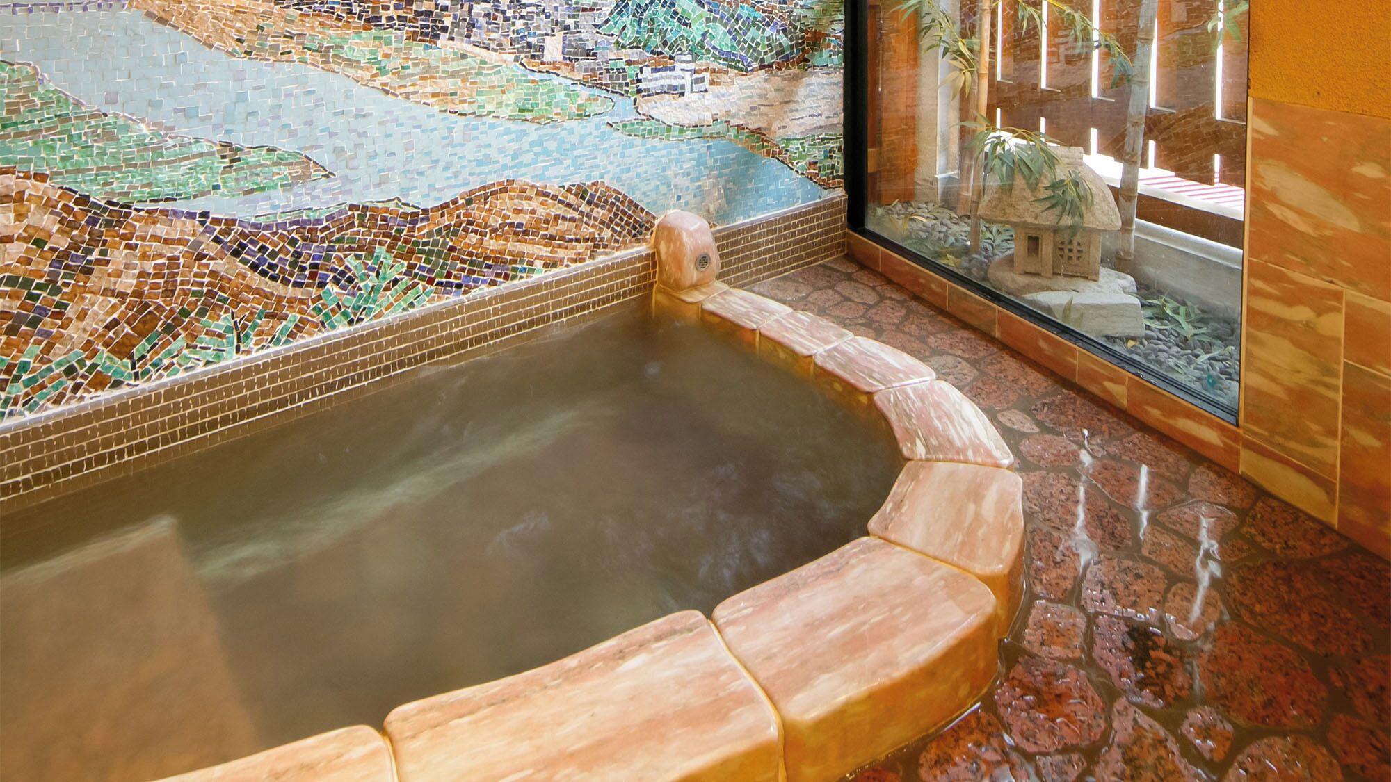 A hot tub with mosaic tiles, a glass enclosure, and a stone floor.