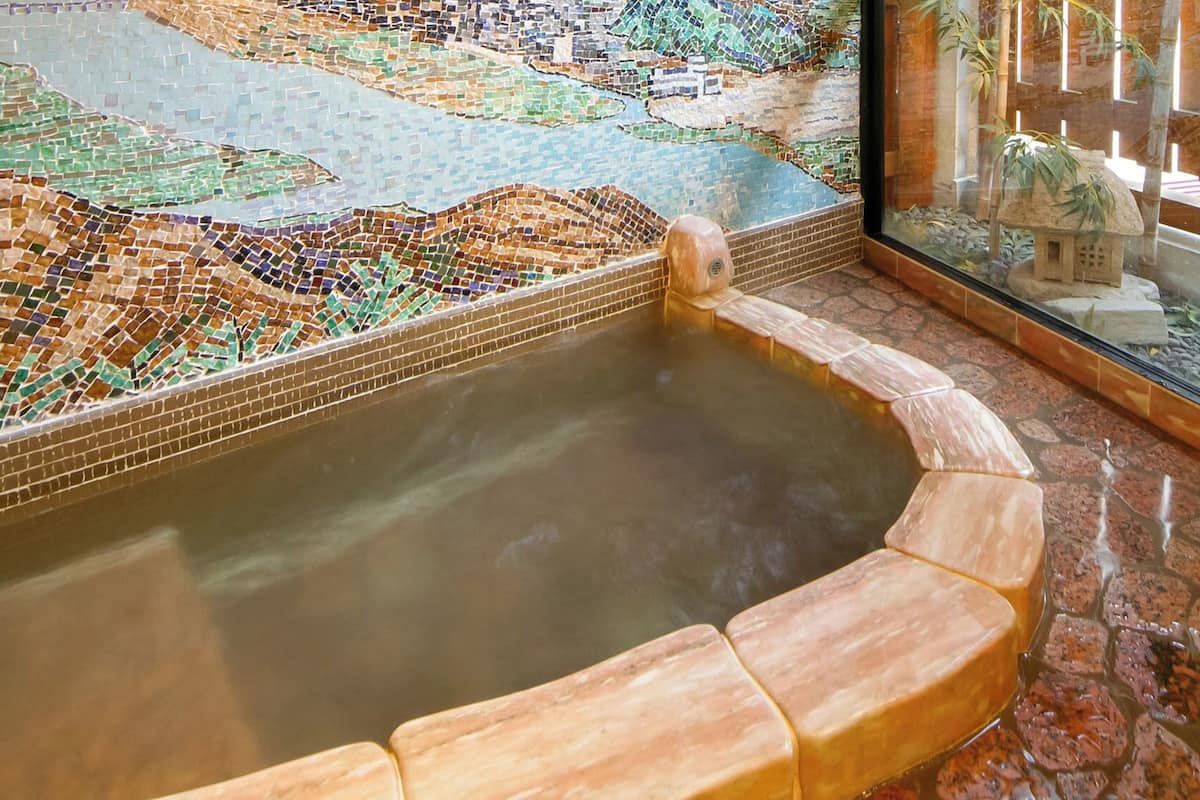 Un jacuzzi con mosaicos, cerramiento de vidrio y suelo de piedra.