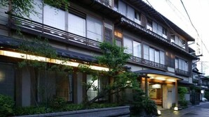 Een traditioneel Japans gebouw met meerdere verdiepingen, grote ramen en een verzorgde tuin ervoor.