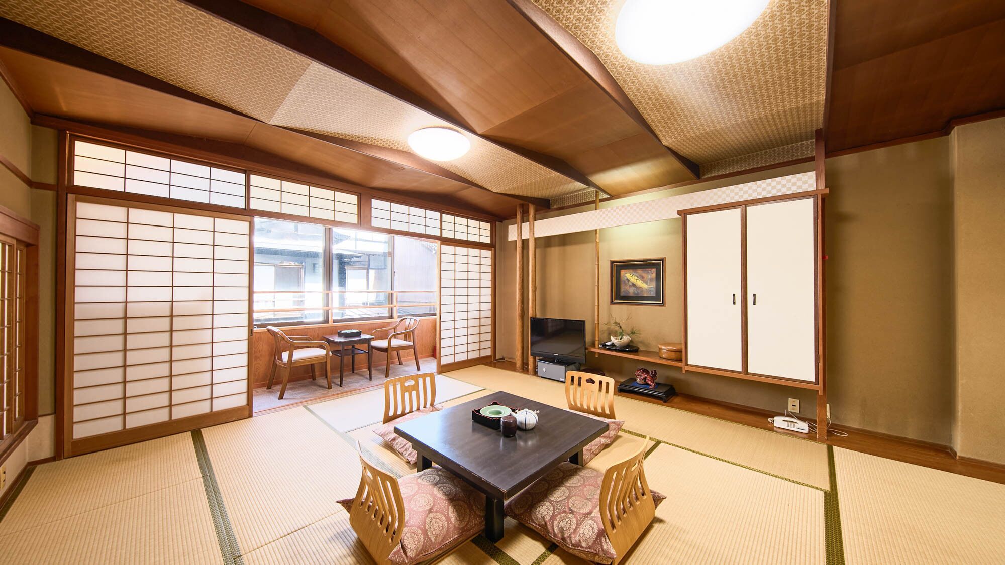 A traditional Japanese room with tatami flooring, a low table with cushions, a television, and sliding doors.