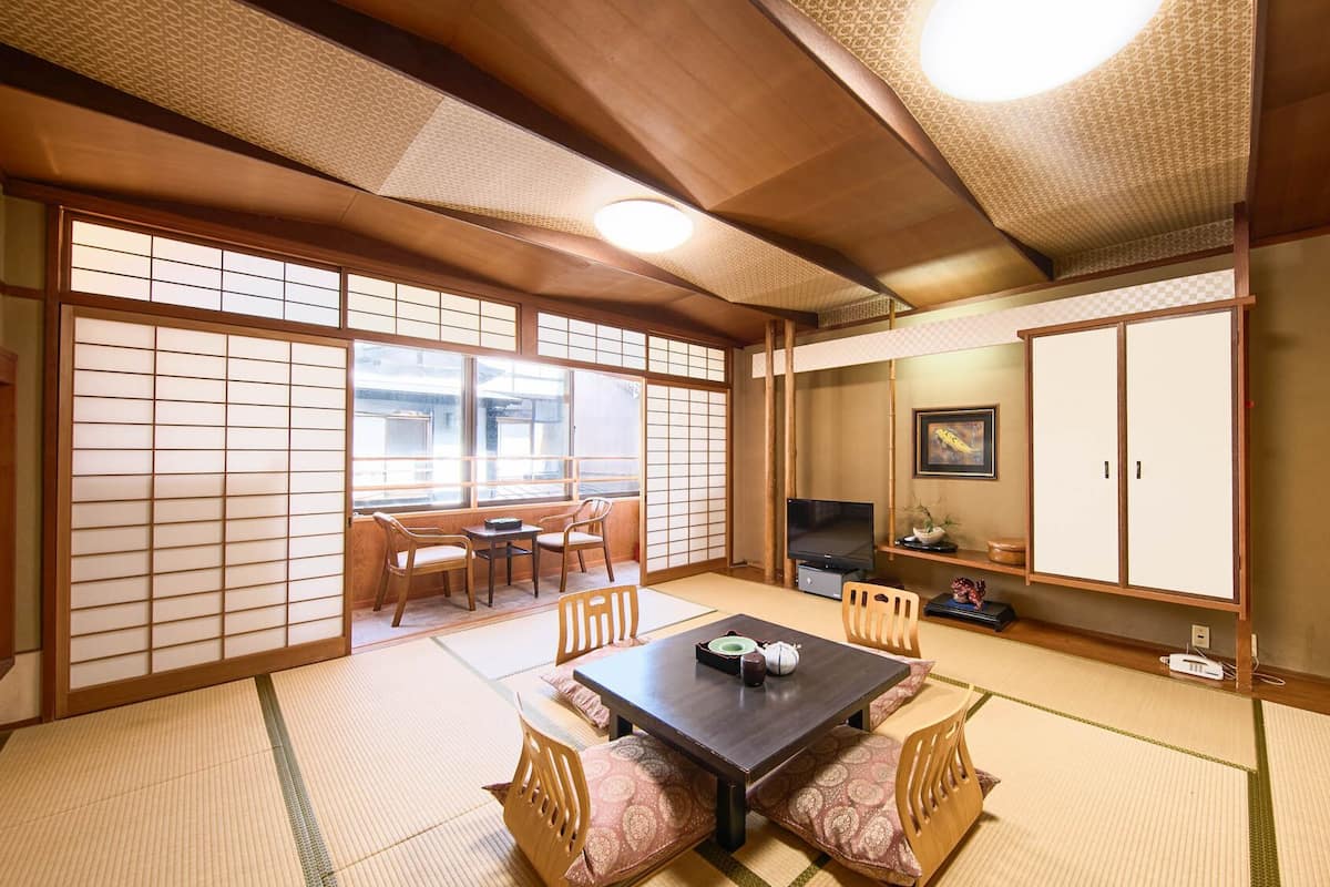 Una habitación japonesa tradicional con suelo de tatami, una mesa baja con cojines, un televisor y puertas correderas.