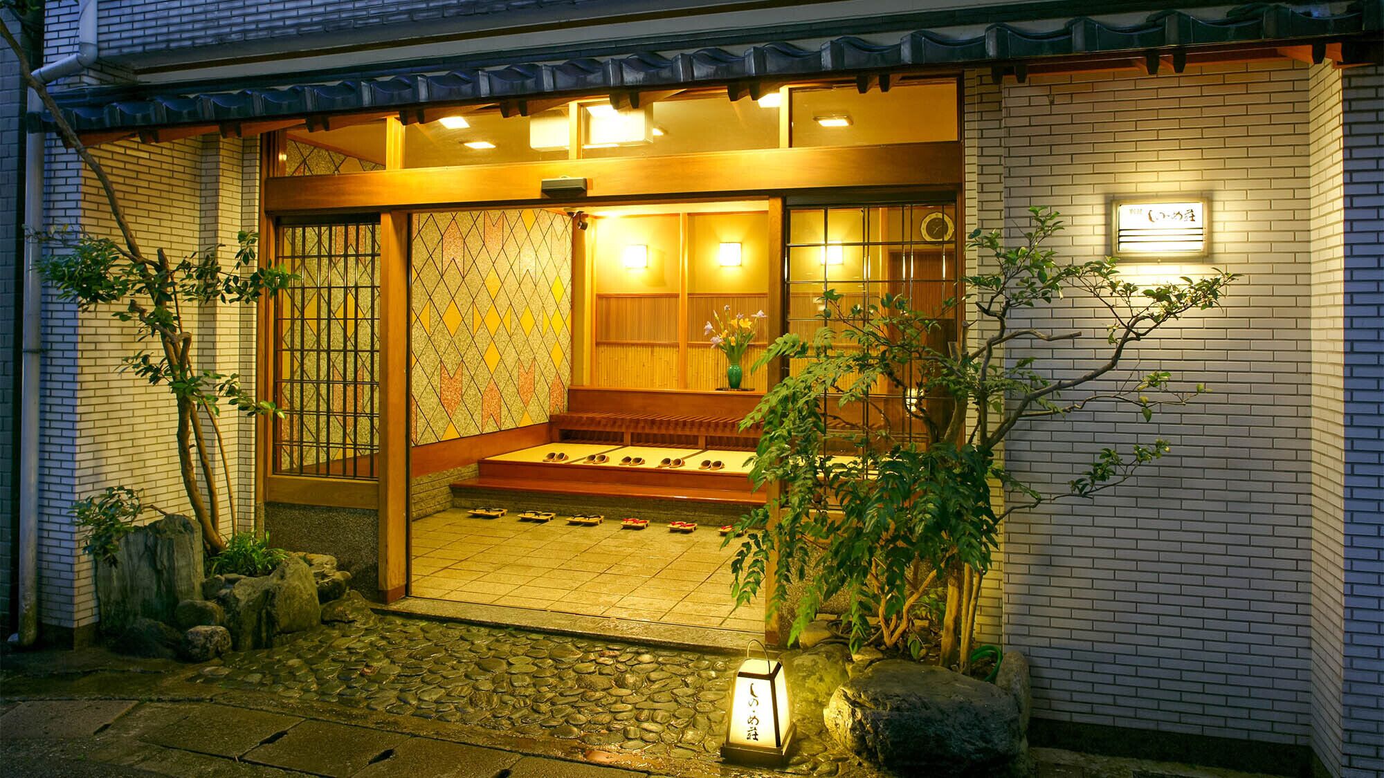 A traditional Japanese building with a wooden entrance, tatami mat flooring, and a small garden area with rocks and plants.