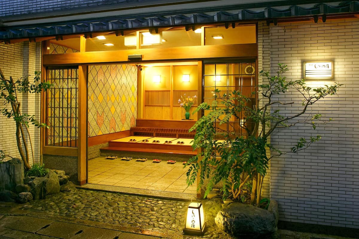 Un edificio japonés tradicional con entrada de madera, suelo de tatami y un pequeño jardín con rocas y plantas.