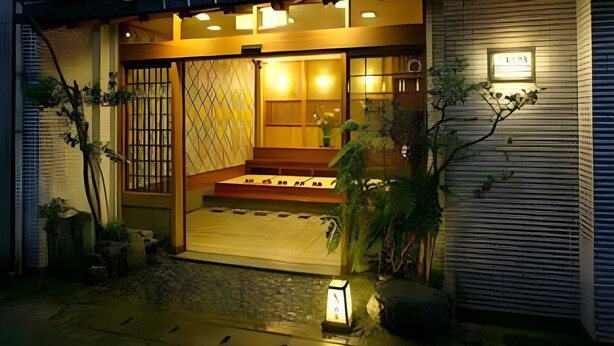 Een traditionele Japanse woning met een houten gevel, een betegelde entree en een kleine tuin met planten en een lantaarn.