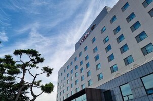 Un moderno edificio de hotel con cielo despejado y un pino al frente.