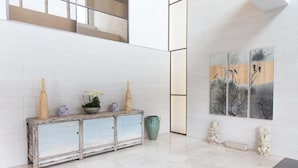 Un vestíbulo moderno con piso de baldosas blancas, una consola de madera rústica con objetos decorativos y una obra de arte en la pared que representa pájaros.