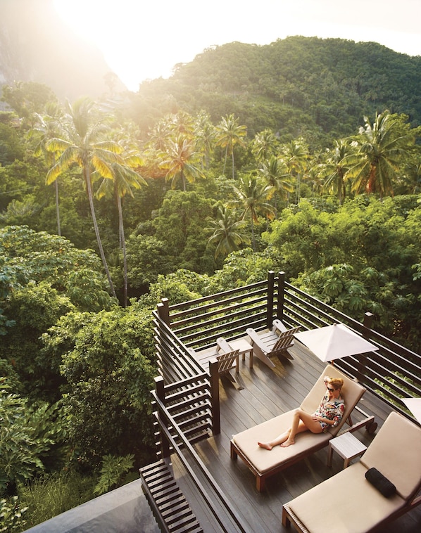 A deck with lounge chairs and an umbrella, surrounded by lush greenery and palm trees. - Boucan BY Chocolat Hotel (Soufrière)