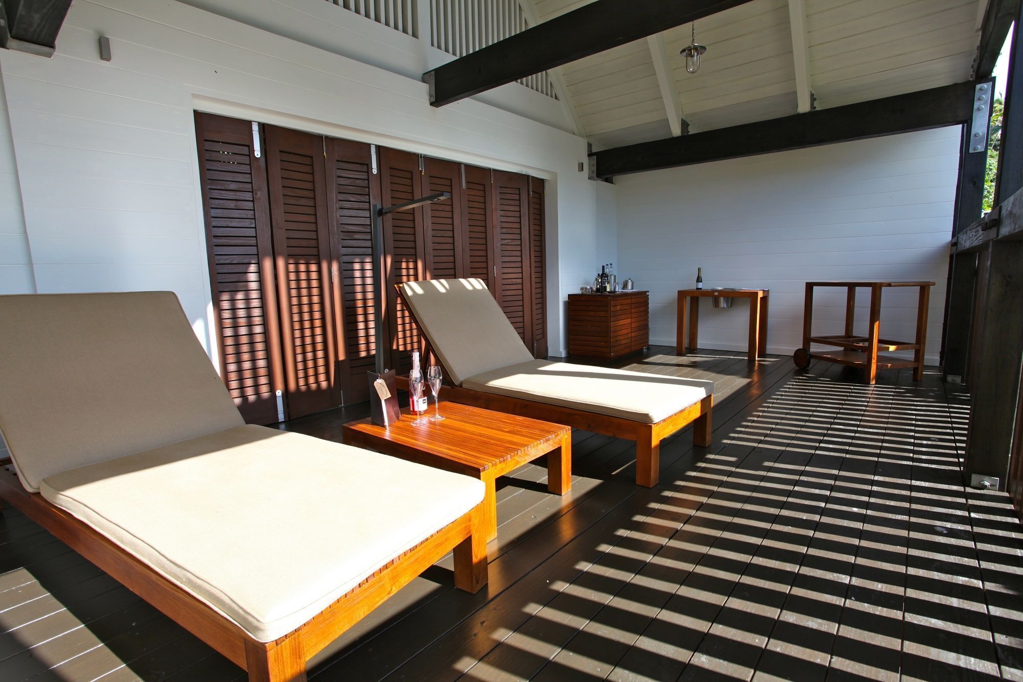 A sunlit room with two wooden lounge chairs, a small wooden table, and a tiled floor.