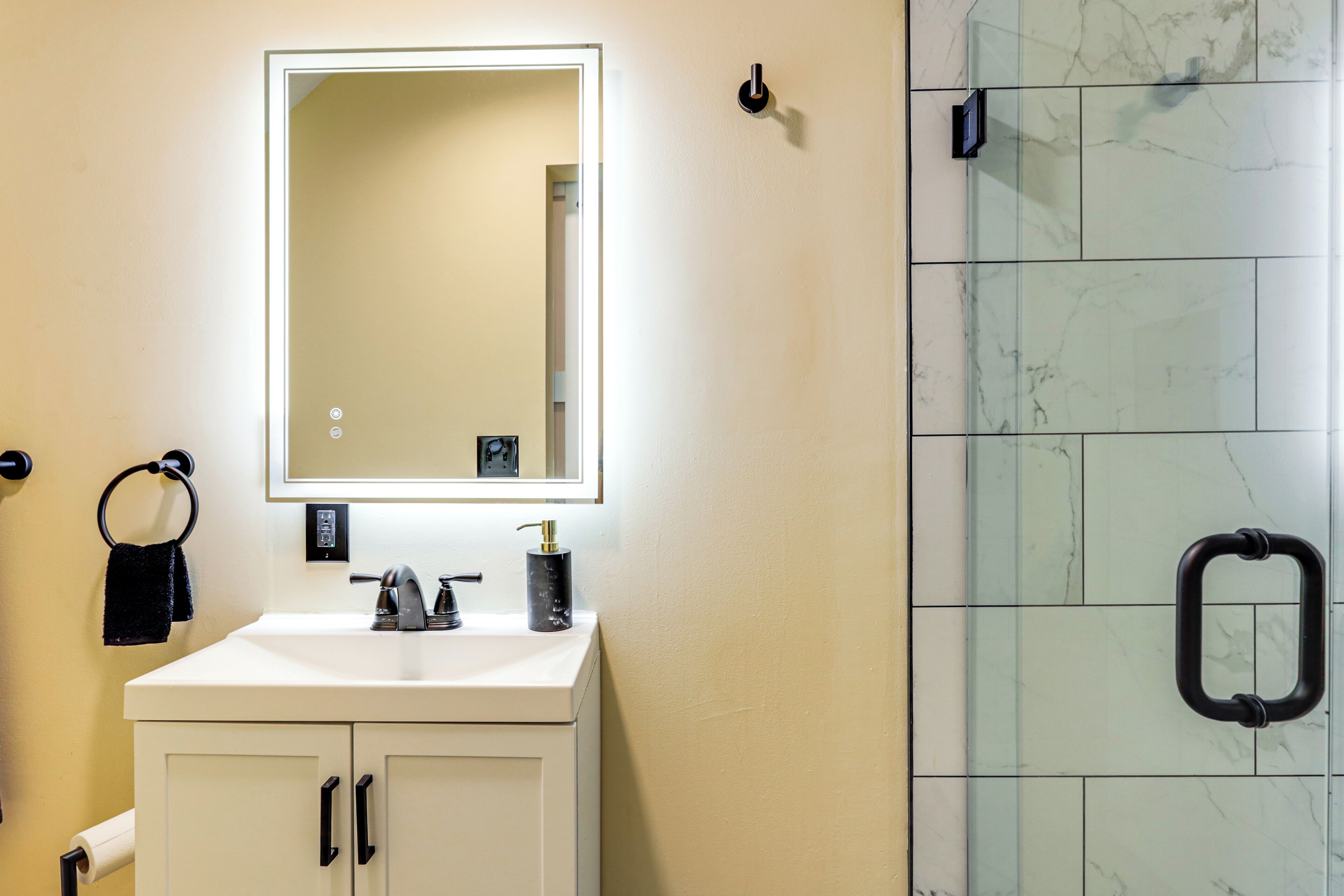 Un baño con un lavabo blanco, un espejo, un perchero para toallas y una cabina de ducha de vidrio.