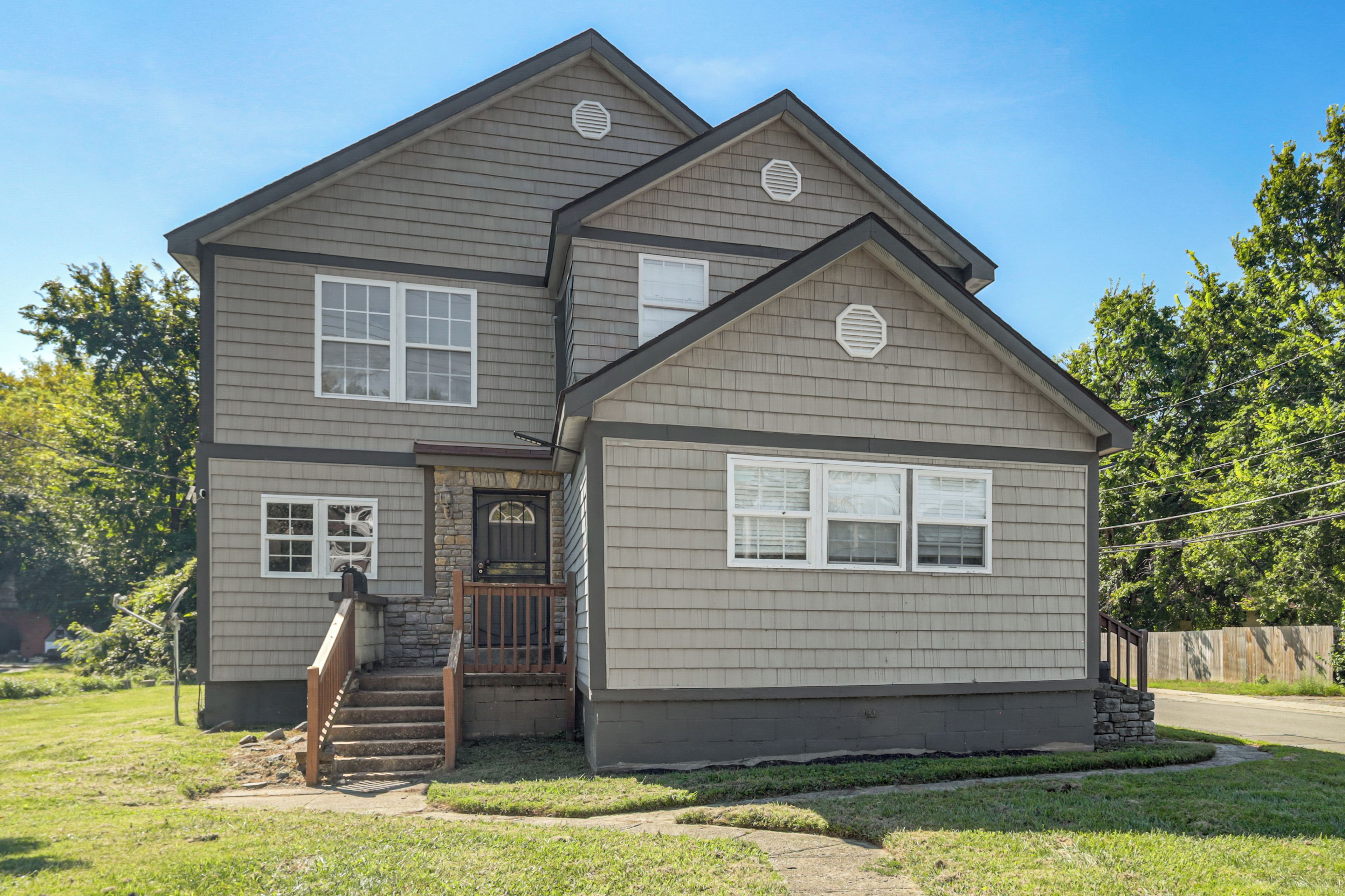 A two-story house with a front porch, a stone entrance, and a small front yard.