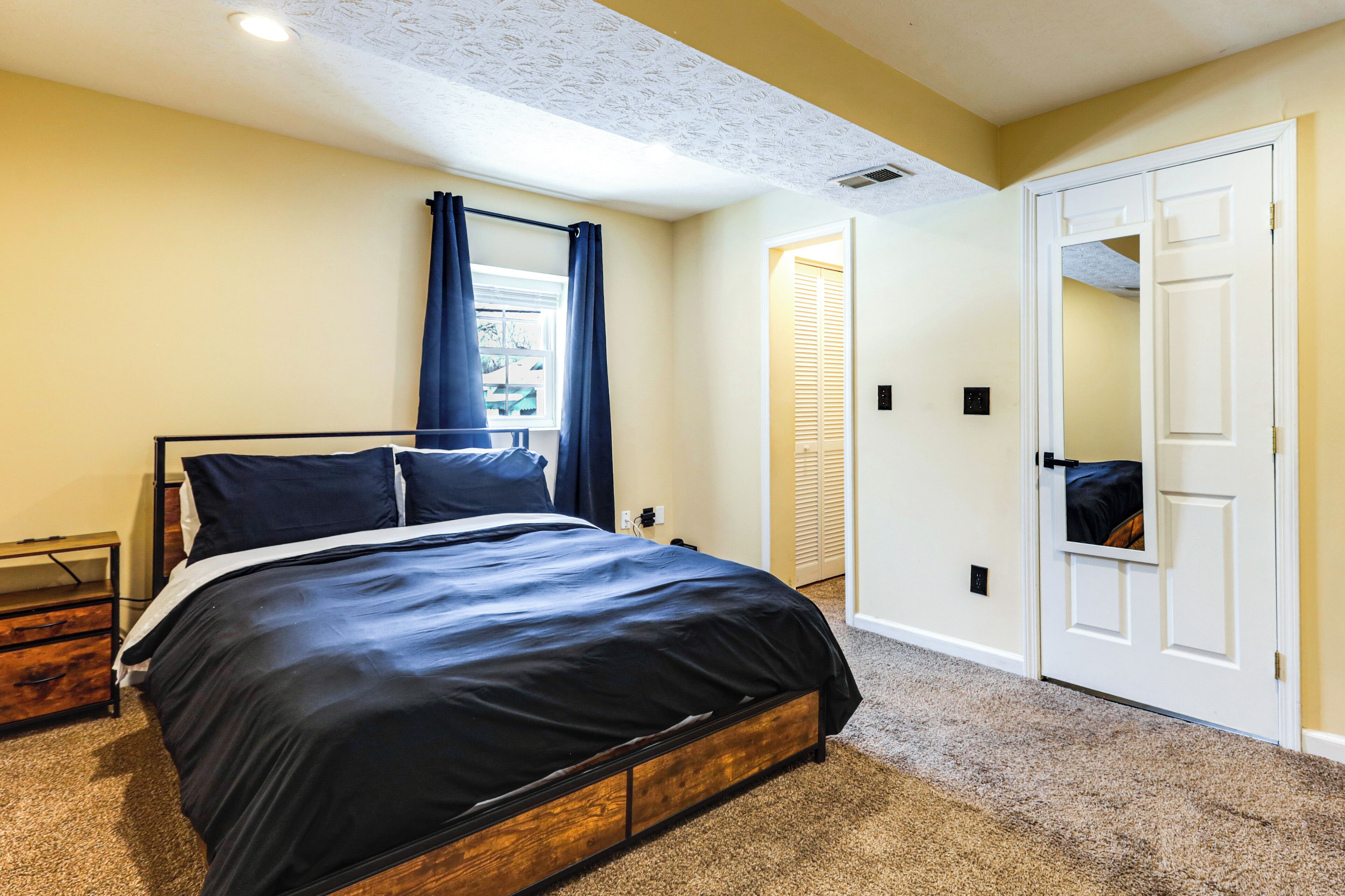 A bedroom with a bed, a window with curtains, a door, and a carpeted floor.