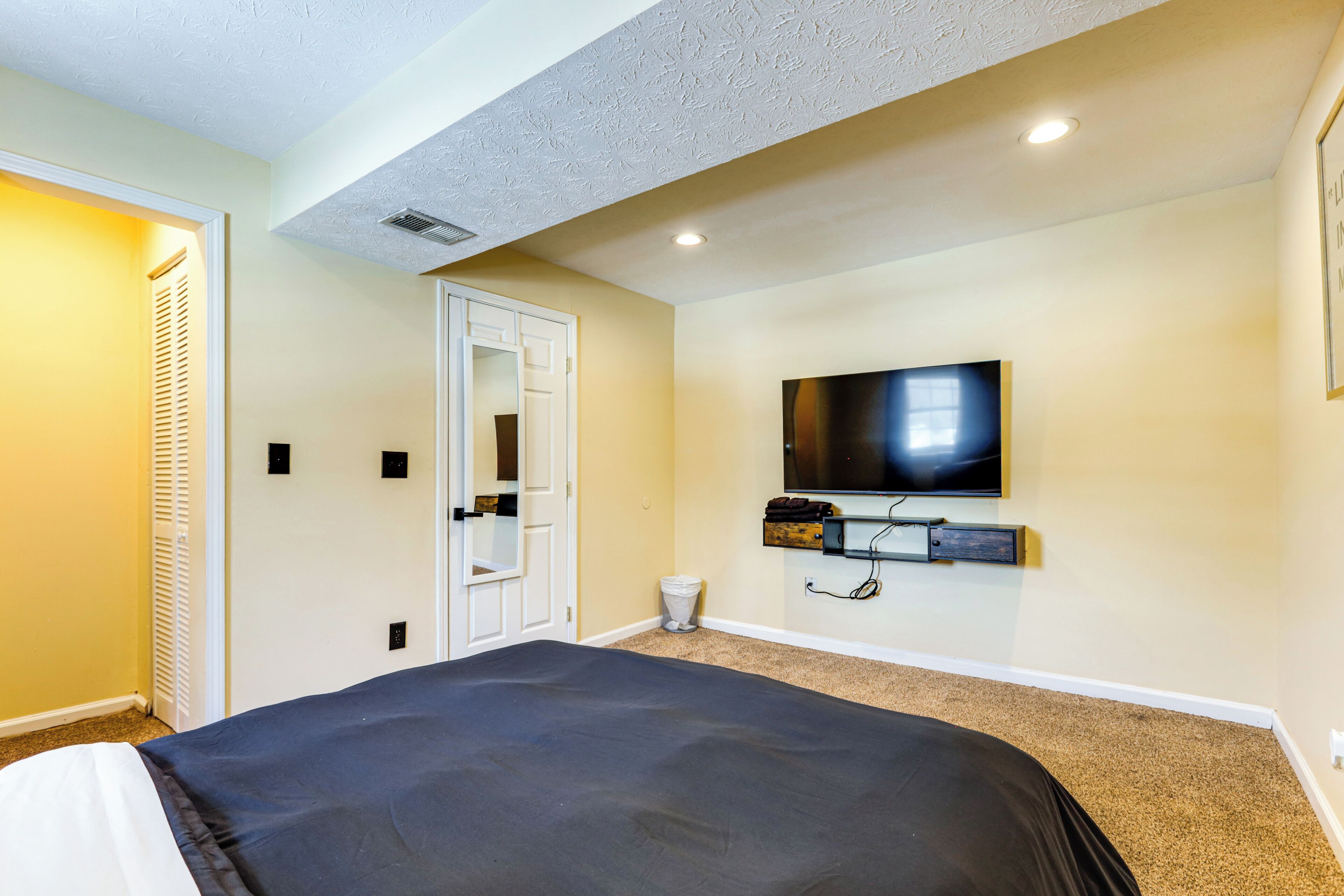 A bedroom with a bed, a television mounted on the wall, and a door leading to another room.