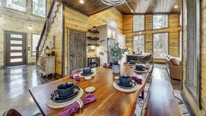 Una cabana espaiosa de fusta amb una gran taula de dinar preparada per a quatre, una zona de cuina i un espai d'estar acollidor amb una llar de foc.