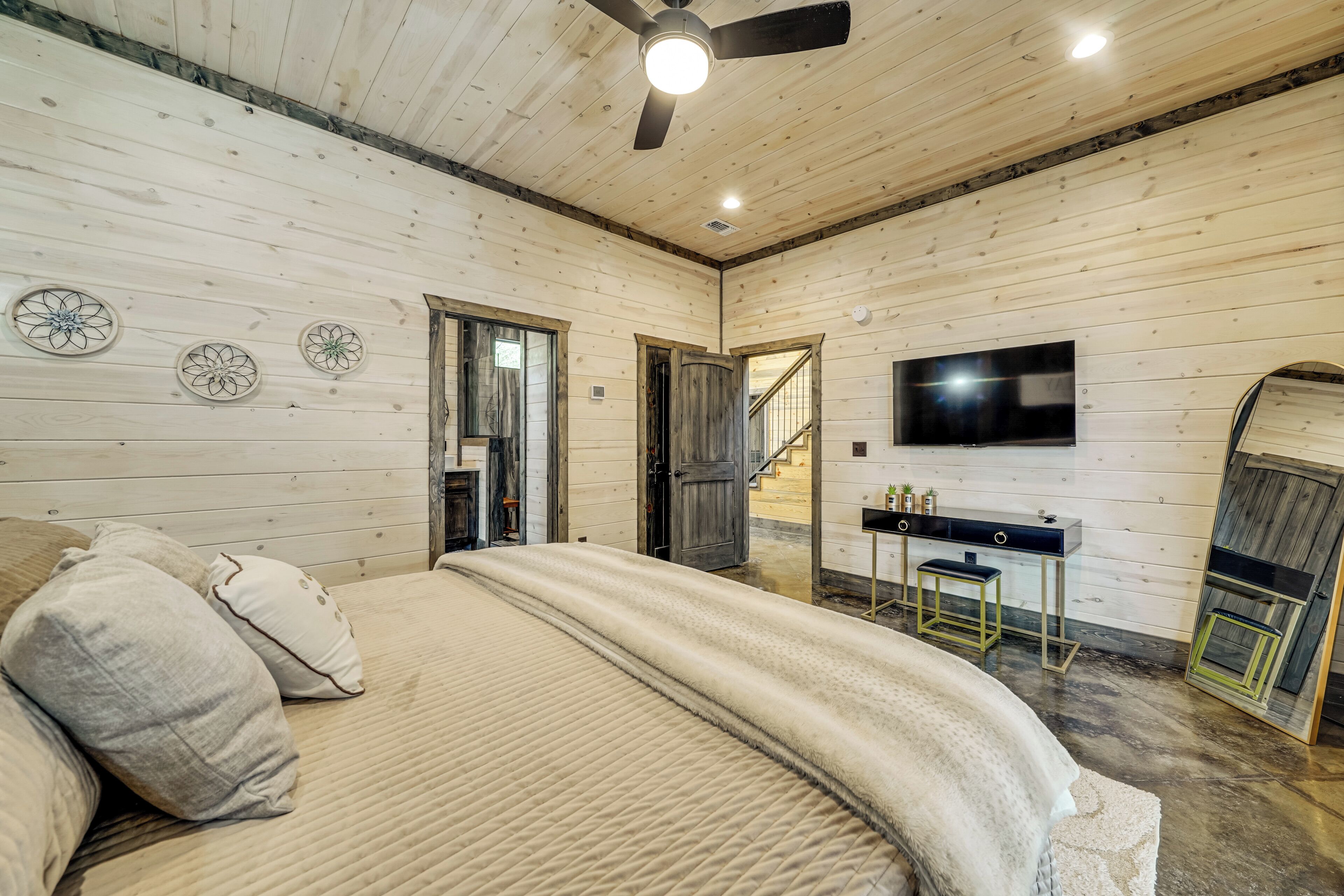 Een slaapkamer met een bed, een plafondventilator, een televisie en een bureau met stoel.