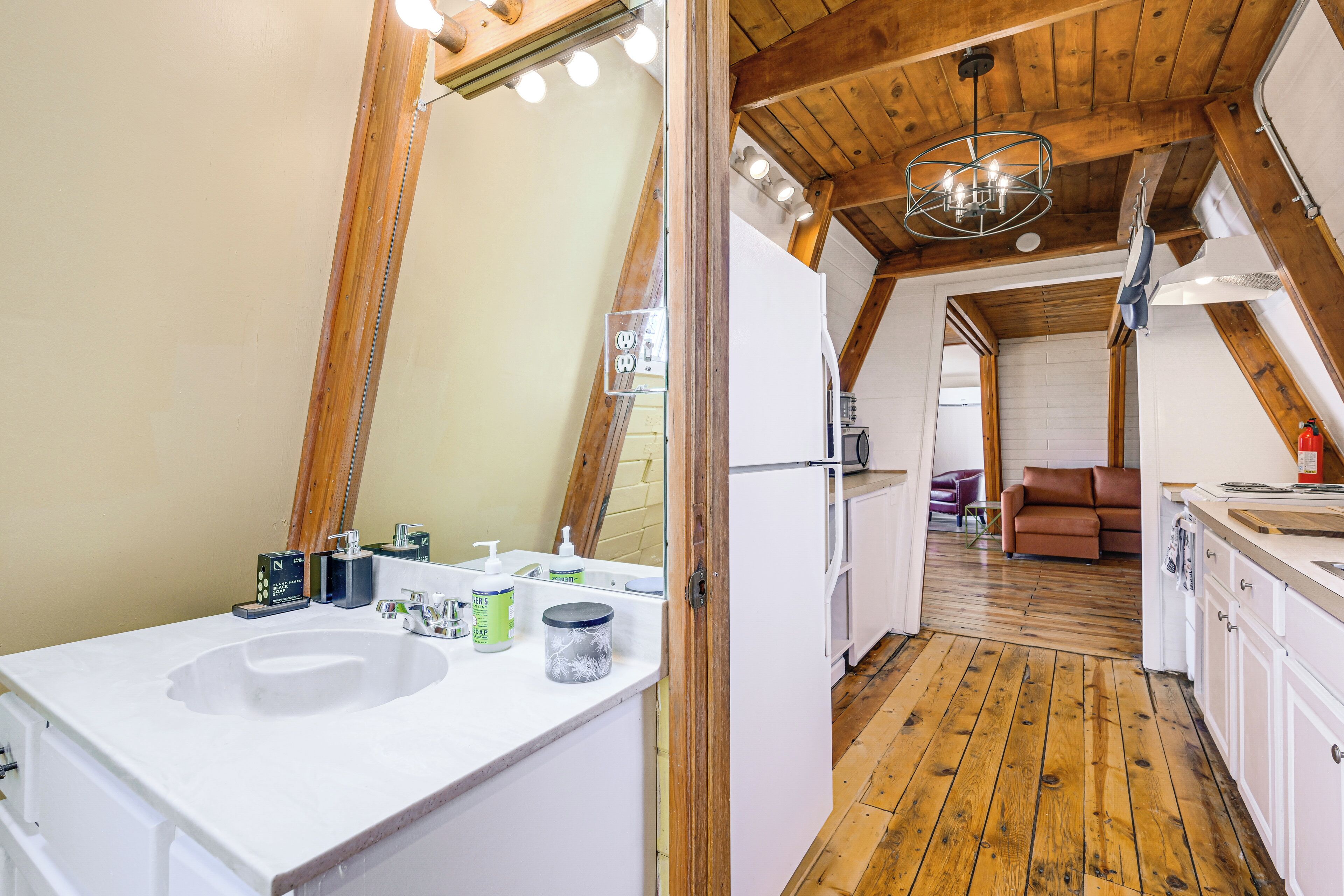 Un baño con un espejo grande, vigas de madera en el techo y un lavamanos con artículos de aseo.