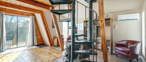 A spacious loft with a spiral staircase, wooden beams, a fireplace, and a large window.