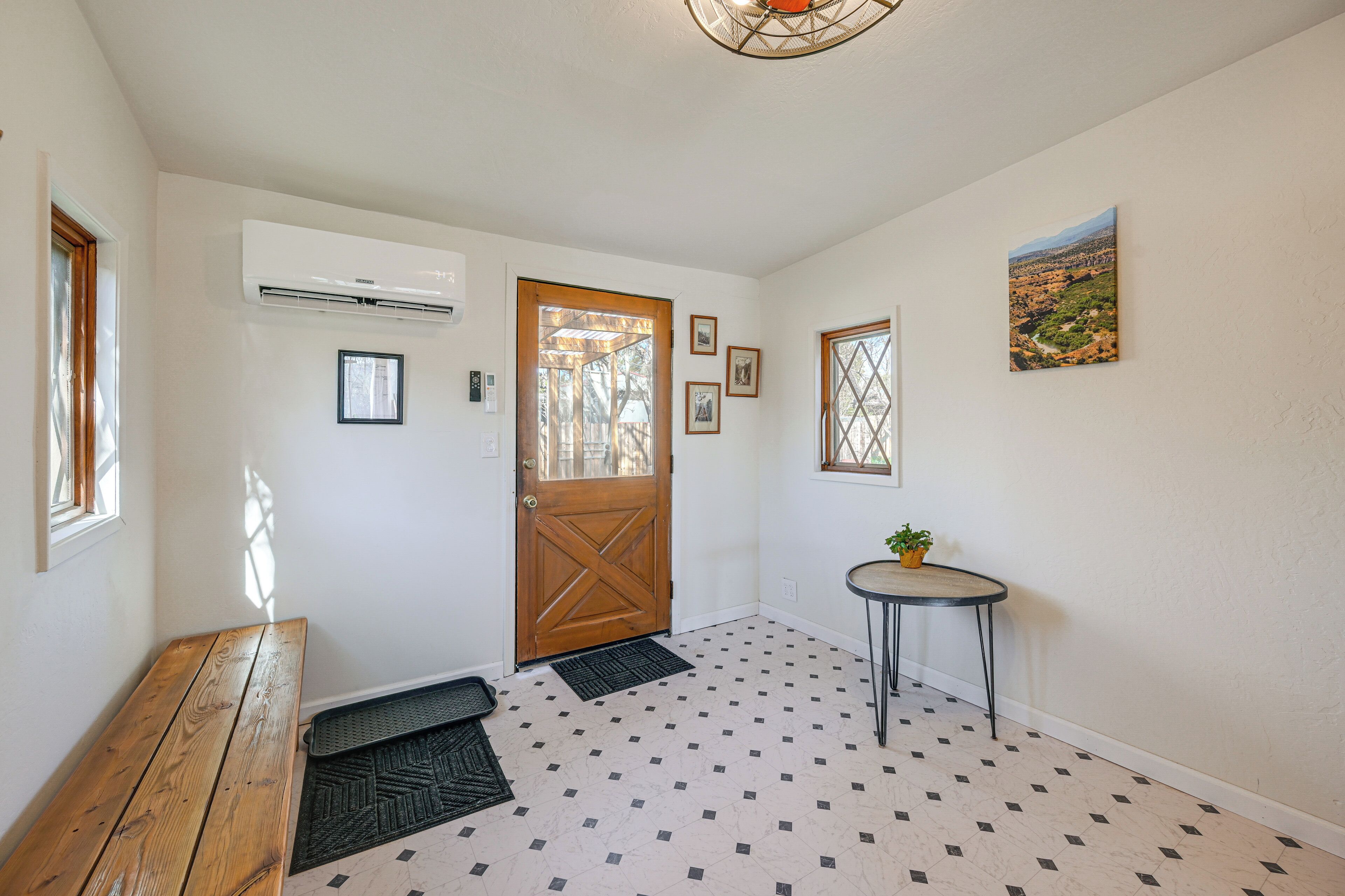 A hallway with a wooden bench, a door, a small table with a plant, and a patterned floor.