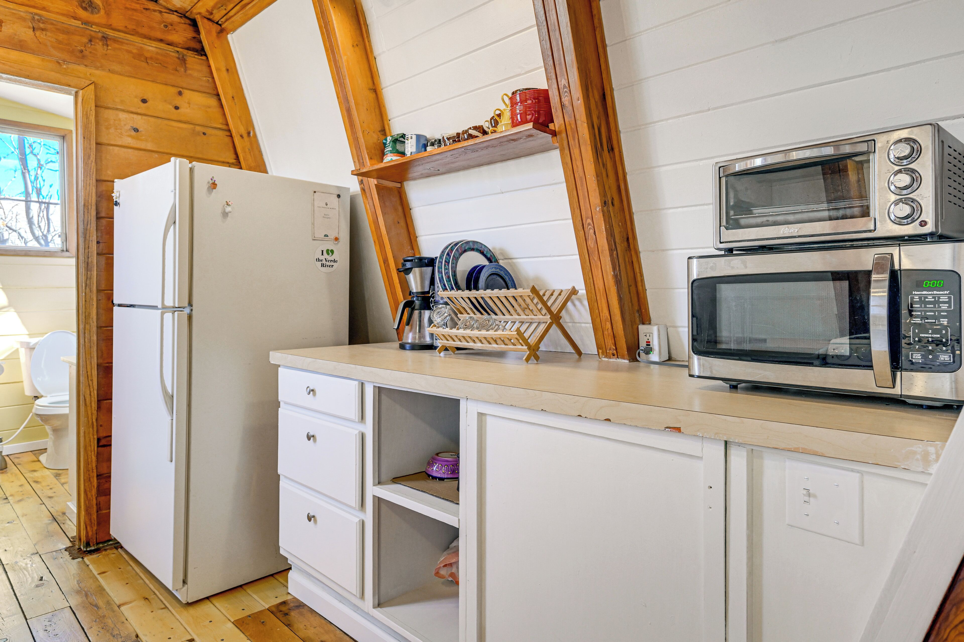 A compact kitchen with a refrigerator, microwave, and wooden shelves.