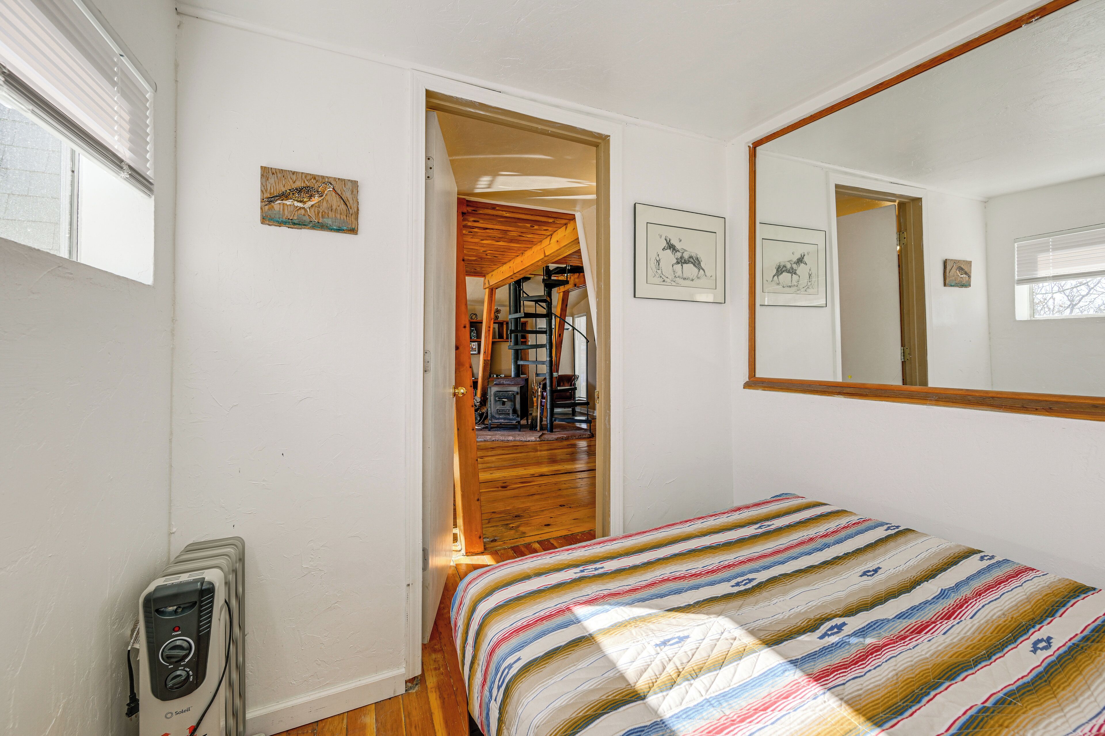 A bedroom with a bed, a wooden floor, a window, a door, and a wall-mounted heater.