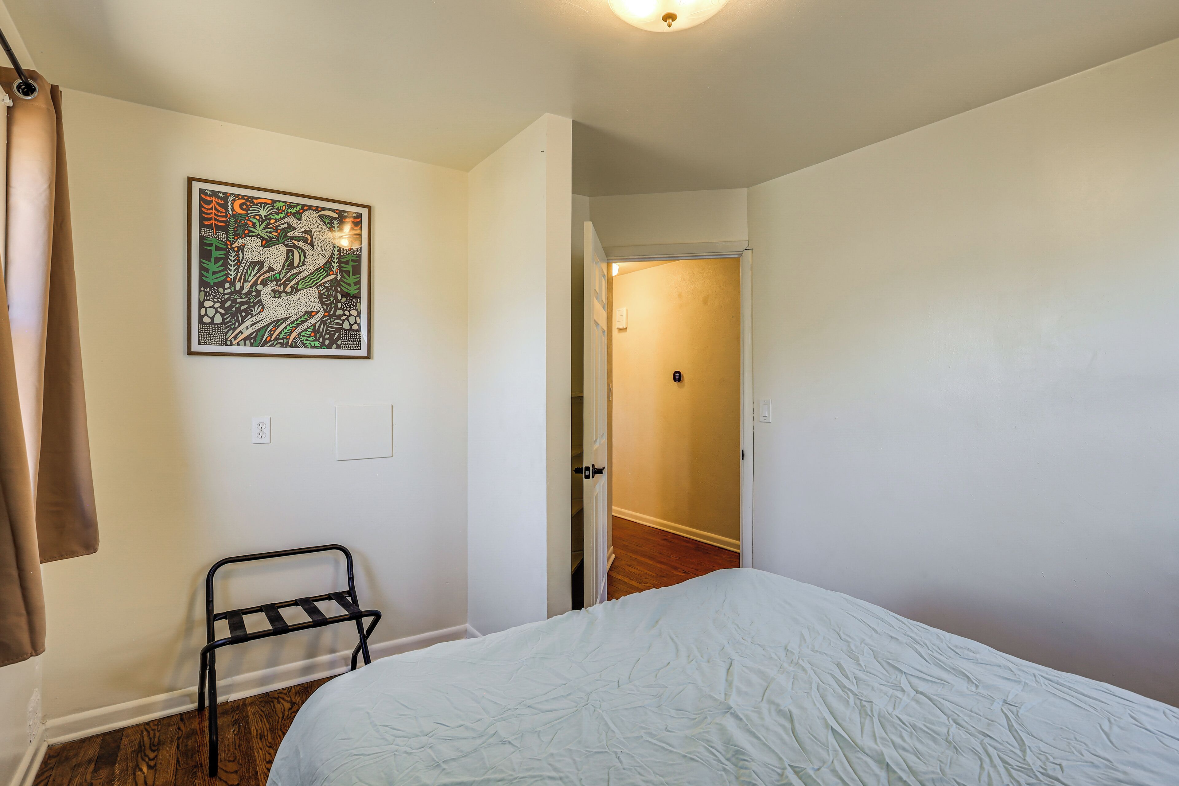 A bedroom with a bed, a metal rack, a door leading to another room, and a wall-mounted picture.