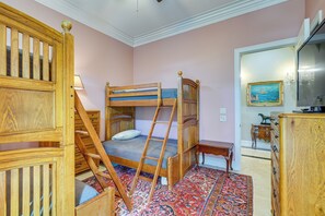 Ein Zimmer mit einem Etagenbett, einer Holzleiter, einem Schreibtisch, einem Stuhl, einer Kommode und einem Bild an der Wand.