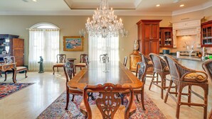 A spacious dining area with a large wooden table, ornate chairs, a chandelier, and a kitchen in the background. - 'like No Other' in the Panhandle of Florida (Panama City Beach)