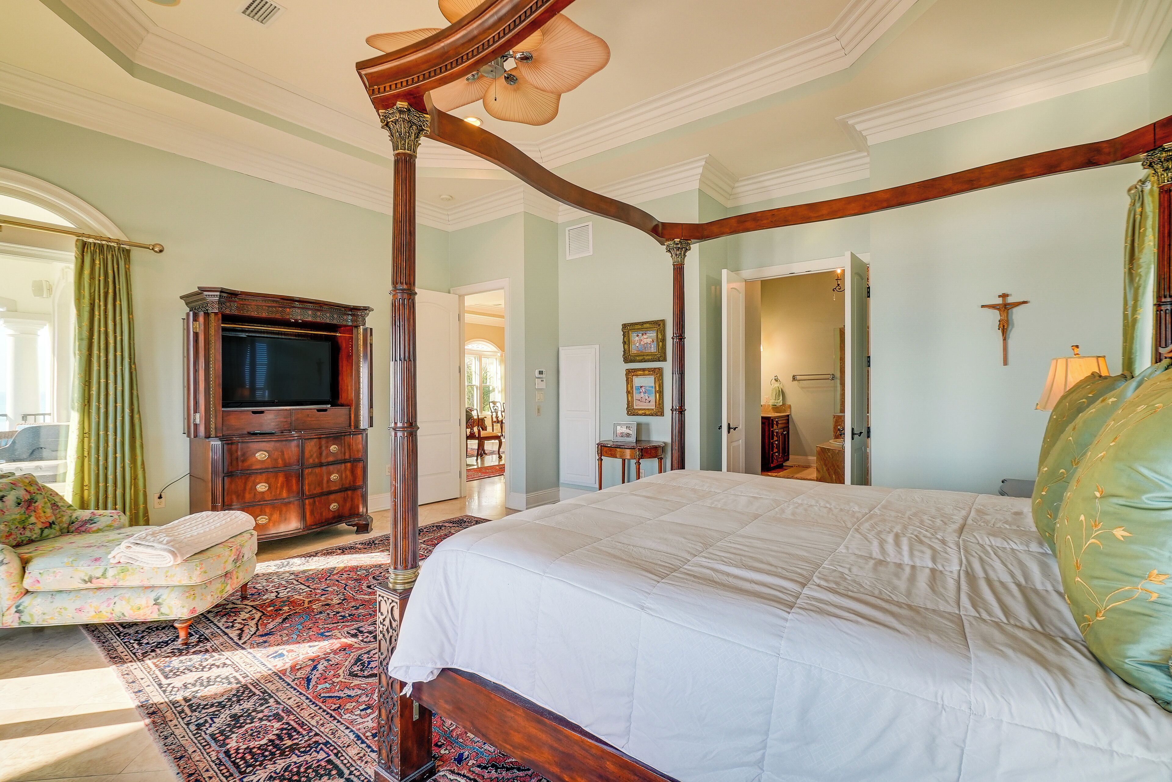 A spacious bedroom with a large bed, a wooden wardrobe, a television, and a floral armchair.