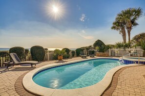Piscina com espreguiçadeiras, uma pequena banheira de hidromassagem e vista para o mar.