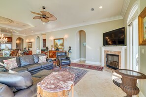 Uma sala de estar ampla com lareira, sofás de couro, uma mesa de centro e uma televisão grande.