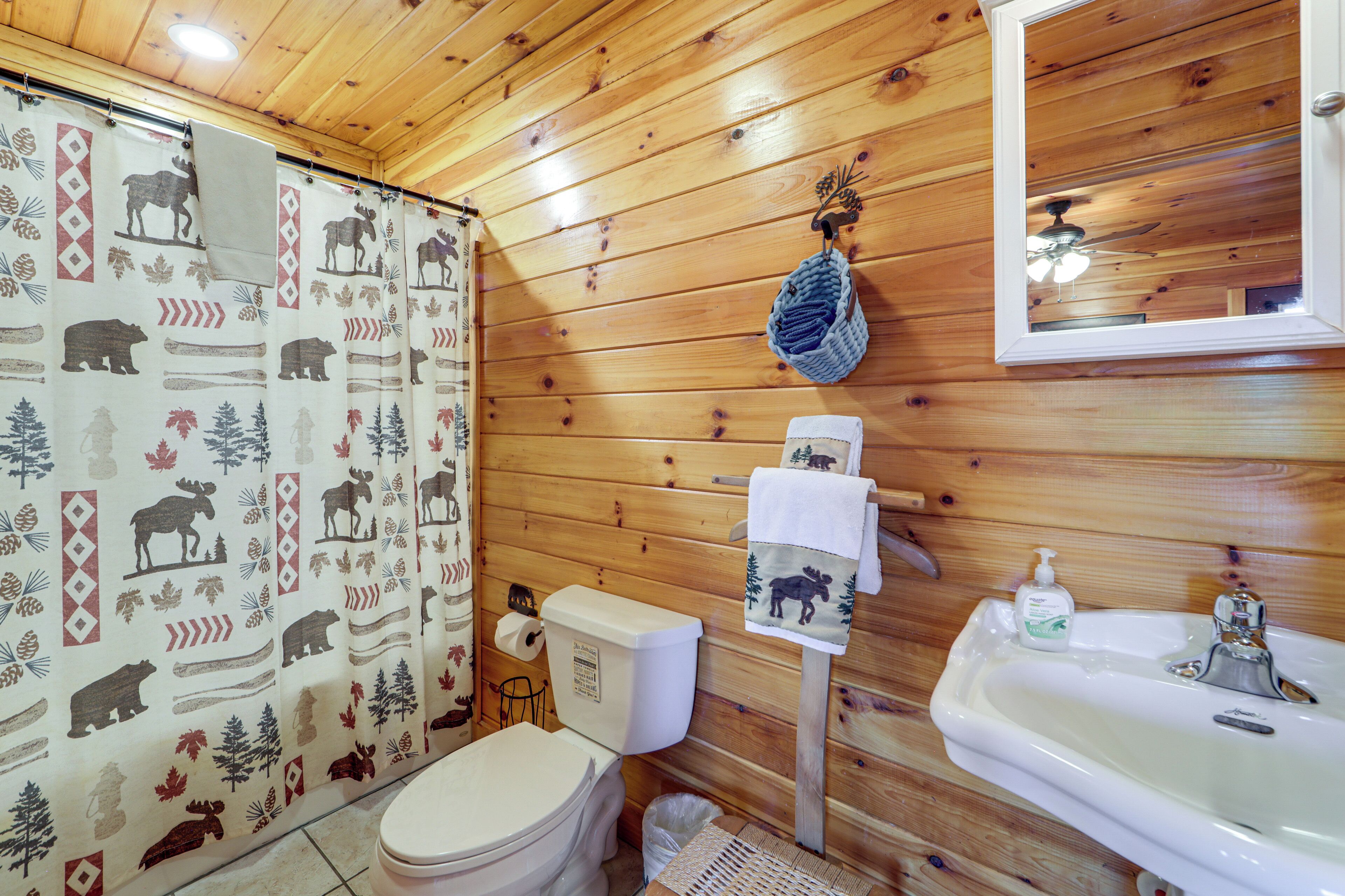 Bagno di una baita in legno con WC, lavandino e tenda da doccia con stampe animalier.