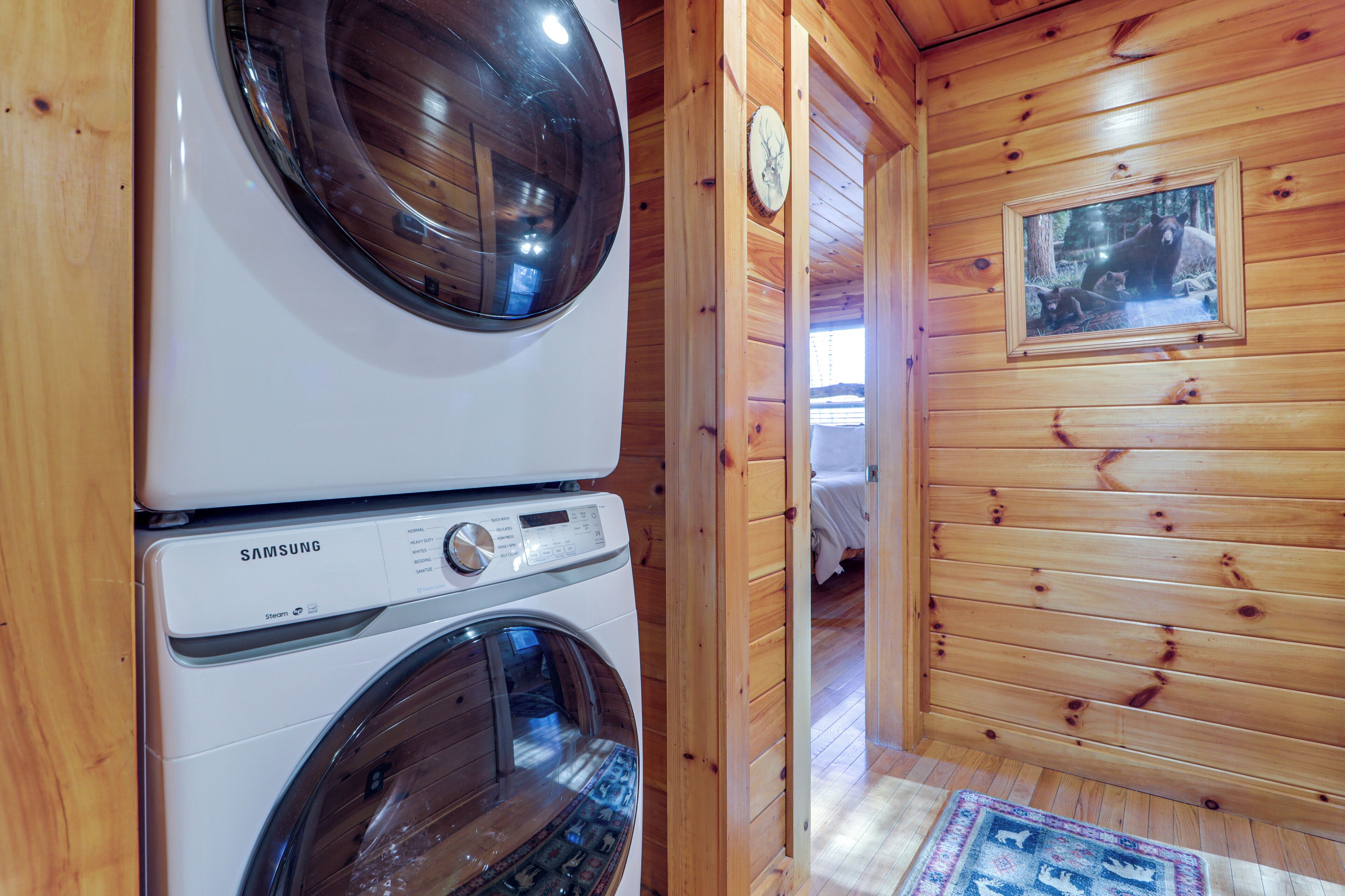 A laundry area with a Samsung washer and dryer, wooden walls, a clock, and a framed picture of bears.