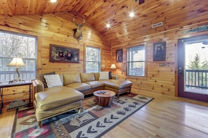 Interior acogedor de una cabaña con un sofá modular, una mesita redonda y una cabeza de venado montada.