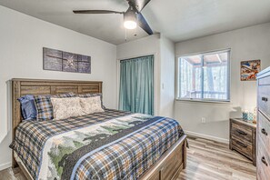 Quarto com cama, ventoinha no teto, janela com persianas e cômoda.