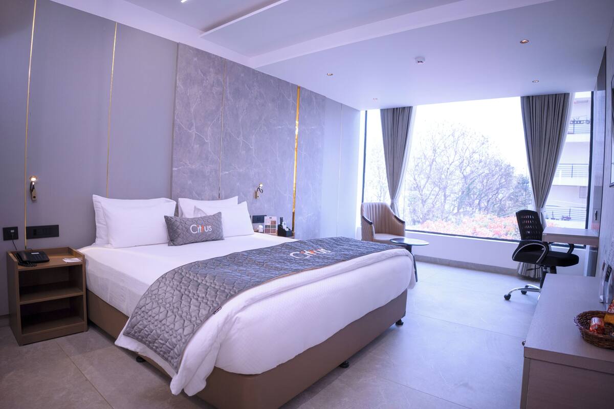 A modern hotel room with a large bed, a desk, a chair, and a view of the outdoors.