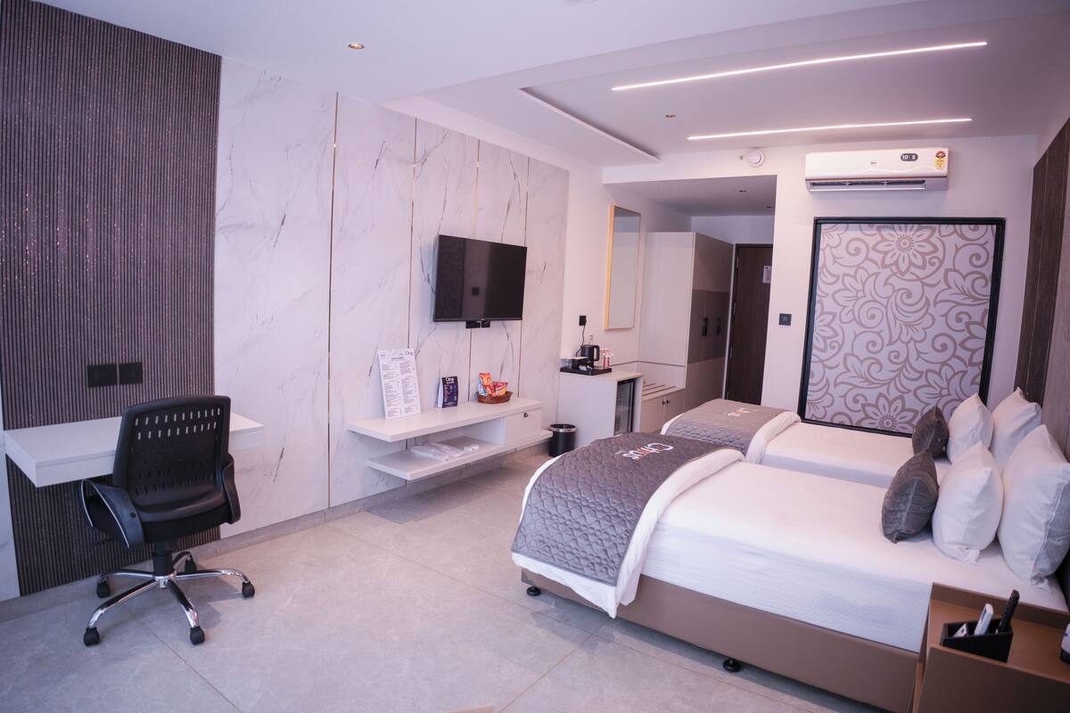A modern hotel room with a bed, desk, chair, TV, and air conditioning unit.